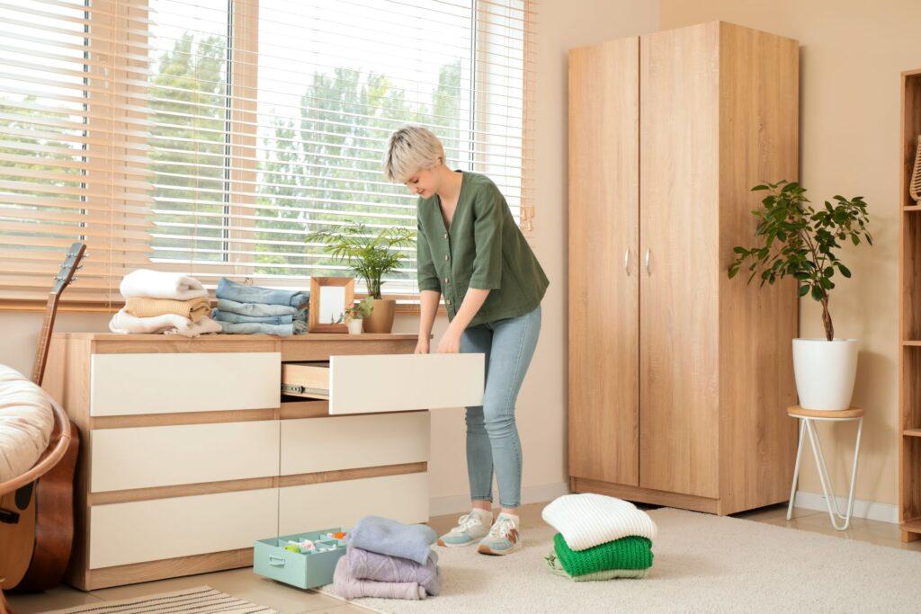 Frau organisiert Kleidung in Schubladenkommode in einem hellen, aufgeräumten Raum mit Holzschränken und Pflanzen für eine gemütliche und funktionale Atmosphäre.