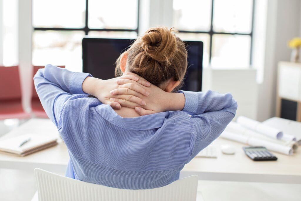 Frau fass sich im Büro mit beiden Händen an den Nacken