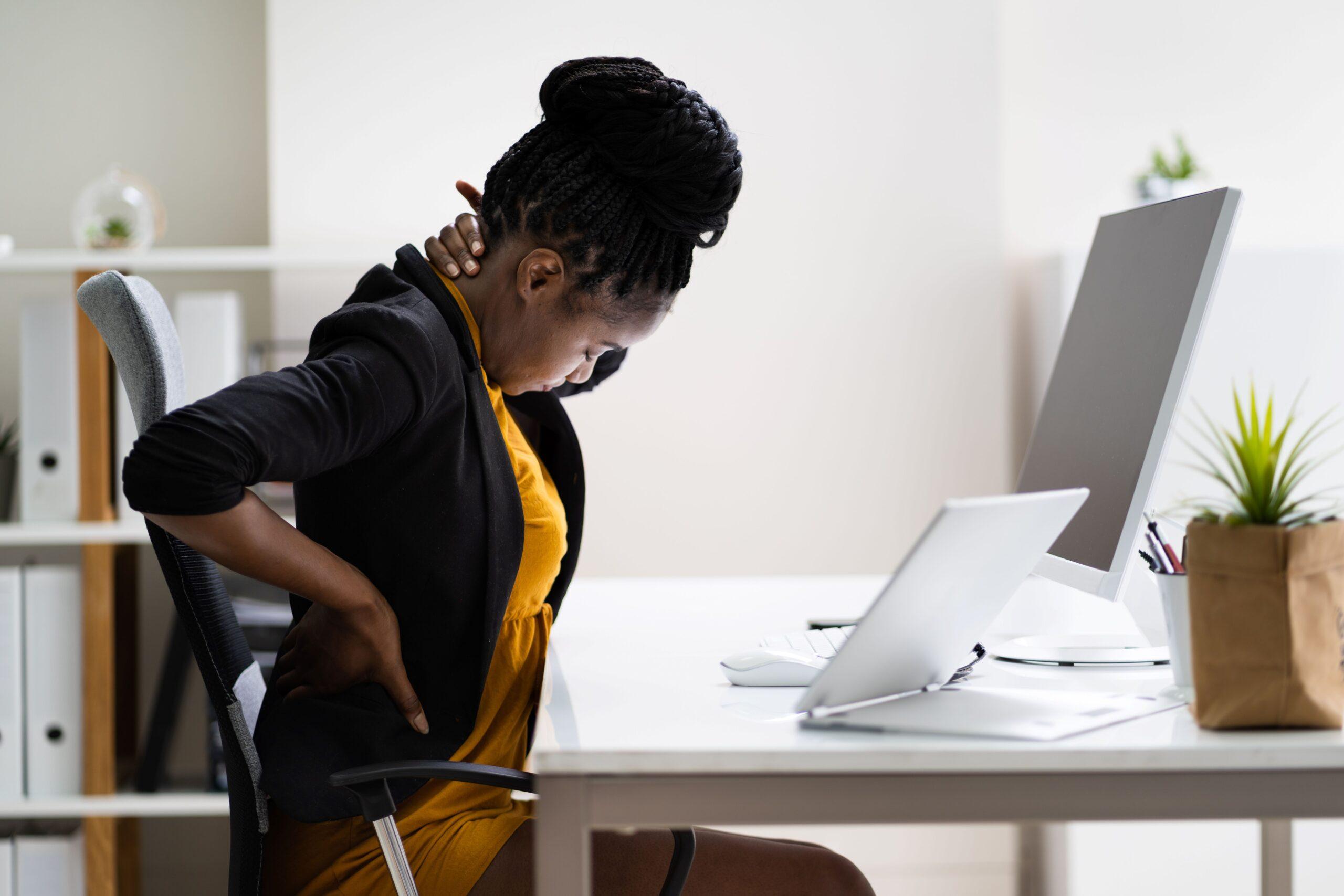 Frau fasst sich im Büro an den Nacken und an den Rücken