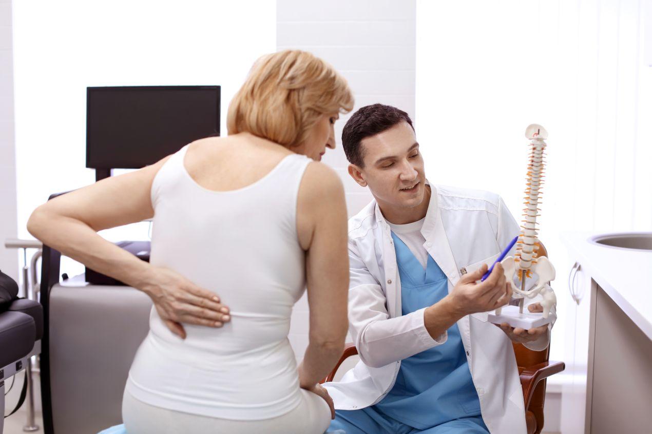 Orthopäde Köln zeigt Patientin mit Rückenschmerzen ein Wirbelsäulenmodell zur Diagnose und Beratung