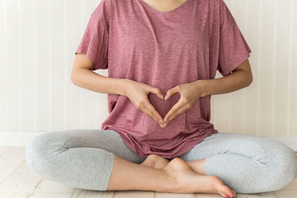 Frau im Schneidersitz formt Herz ueber dem Bauch Symbol fuer gesunde Verdauung mit CURCUMA KAPSELN