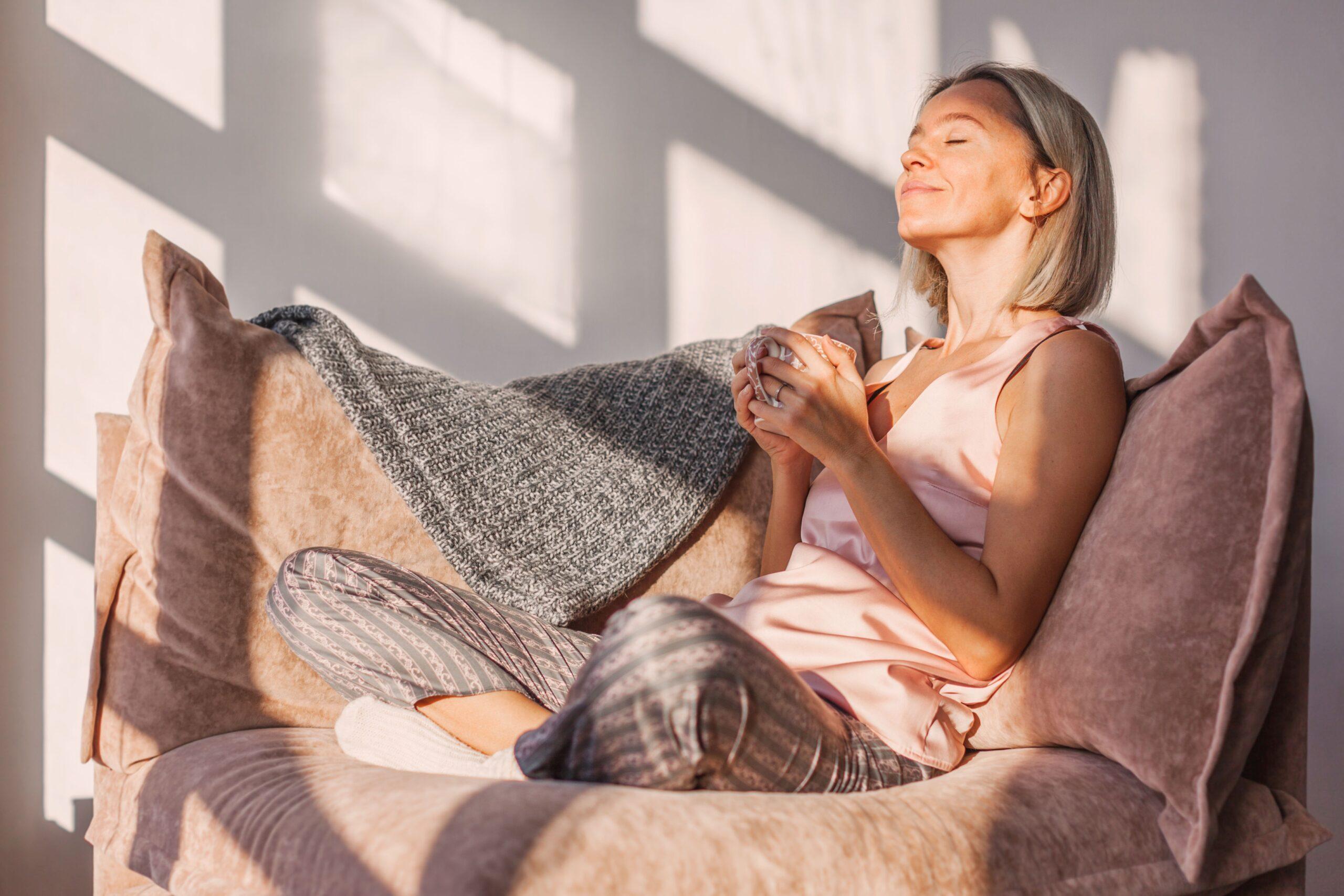 Frau sitzt entspannt auf dem Sofa im Sonnenlicht mit Tasse in der Hand