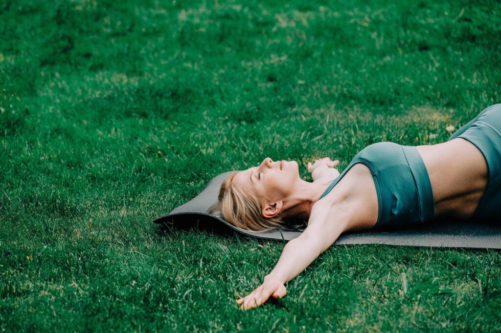 Frau liegt entspannt auf Yogamatte im Gras | Schwenkgrill kaufen